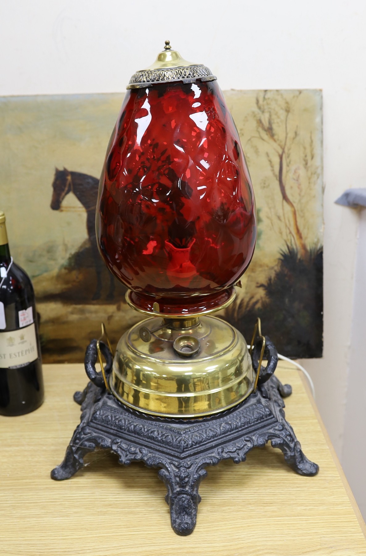 A floor-standing cranberry glass, brass and iron-mounted lamp, converted to a table lamp, 63cms high
